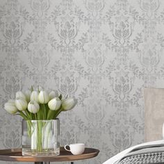 white tulips in a vase on a table next to a bed