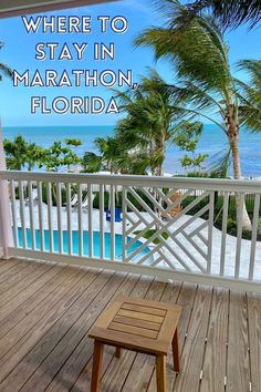 there is a bench on the porch overlooking the water and palm trees in the background