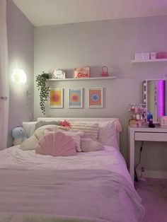 a white bed sitting under a purple light in a bedroom next to a desk and mirror