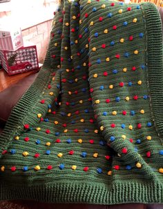 a green blanket with multicolored dots on it sitting on a leather chair next to a wooden table