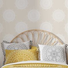 a bed with yellow and white pillows in front of a wallpapered headboard