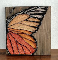 an orange and yellow butterfly wing on a wooden block with beaded trimmings