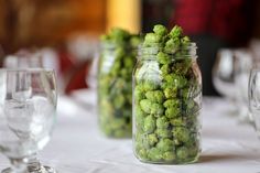 there are many glass jars with green flowers in them on the dining room table set for dinner