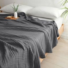 an unmade bed with white pillows and a gray blanket on it, in front of a plant