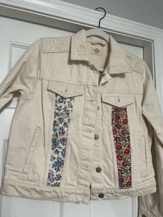 a white jacket hanging on a door with flowers and leaves printed on the front pocket