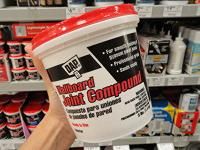 a hand is holding up a cup of paint in a store aisle with other products on the shelves