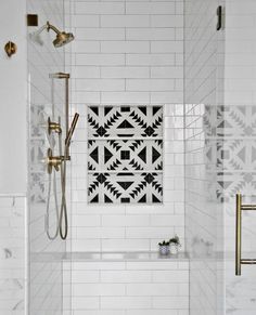 a white tiled bathroom with black and white tiles on the wall, shower head, and bathtub