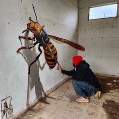 a man kneeling down next to a painting of a bee on the side of a wall