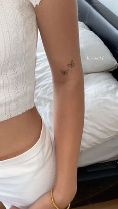 a woman with a small butterfly tattoo on her left arm, standing in front of a bed