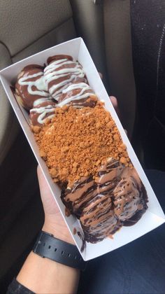 a person holding up a box filled with chocolate covered donuts