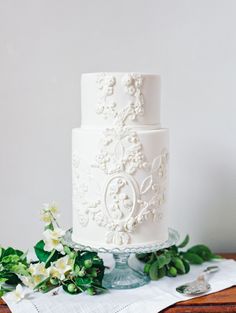 a white wedding cake sitting on top of a table next to flowers and greenery