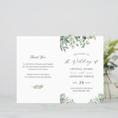 a wedding program with greenery on the front and back, sitting next to a vase filled with flowers