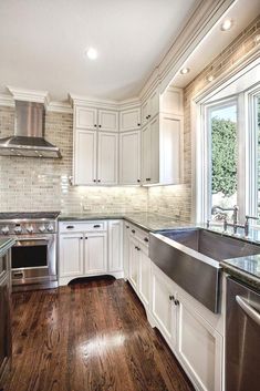 a kitchen with wooden floors and white cabinets, stainless steel appliances and an open window