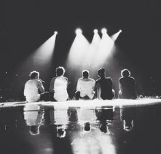 four people sitting on the ground in front of three spotlights with their backs turned