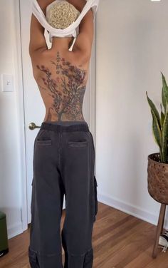 a man with tattoos on his back standing in front of a potted plant and holding onto a rope