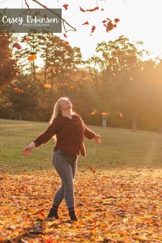 a woman is playing with leaves in the park on a fall day, and she has her arms spread wide open