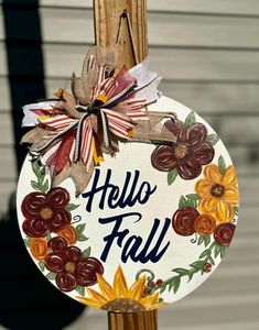 a sign that says hello fall hanging from a wooden post with flowers painted on it