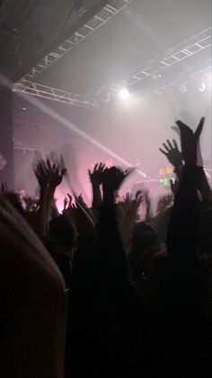 a crowd of people at a concert with their hands in the air and lights on