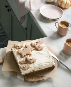 there is a cake with icing and decorations on the table next to two mugs