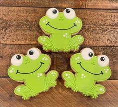 four decorated frog cookies sitting on top of a wooden table