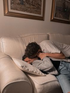 a man laying on top of a white couch under a blanket next to a wall