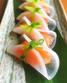 there are many small pieces of sushi on the long green platter with sauce and garnishes