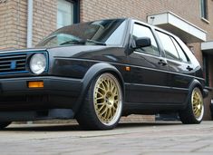 a black car with gold rims parked in front of a brown brick building on the street