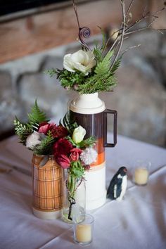 two vases with flowers and greenery on top of a table next to candles