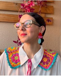 a woman wearing glasses and a colorful crochet scarf with flowers hanging from her head