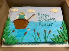 a birthday cake in the shape of a boat with a fisherman on it, sitting in a cardboard box