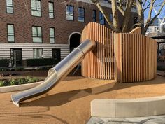 a metal slide in front of a brick building with trees and buildings behind it on the other side