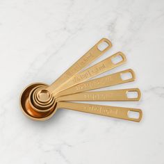 gold measuring spoons with engraved names on them sitting on a white marble countertop