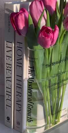 pink tulips are in a clear vase next to two books on a shelf