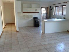 an empty kitchen and living room with tile flooring, white cabinets, and black appliances