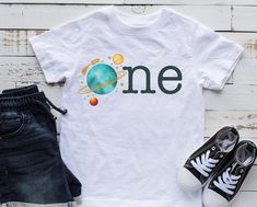 a t - shirt with the word one on it next to some shoes and a pair of jeans