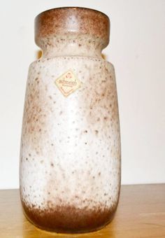 a brown and white ceramic jar sitting on top of a wooden table next to a wall