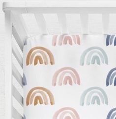 a white crib with rainbows painted on the sheets and pillow cases in pastel colors