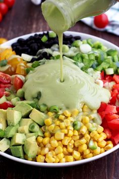 a bowl filled with vegetables and dressing being drizzled over the salad ingredients