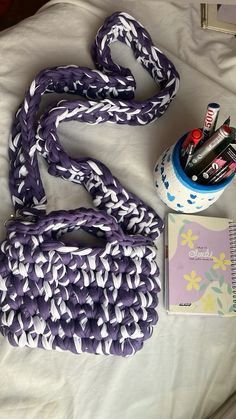 purple and white handbag, notebook, and other items laid out on a bed