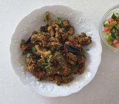 a white plate topped with food next to a bowl filled with veggie salad