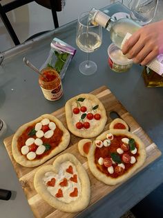 four homemade pizzas with toppings on a cutting board next to bottles of wine