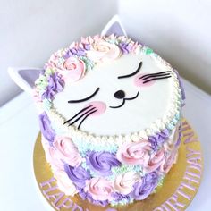 a cake decorated with pink, purple and white frosting has a cat's face on it