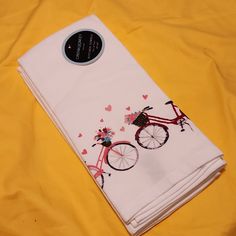 two white towels with bicycles on them sitting on a yellow cloth covered tablecloth,