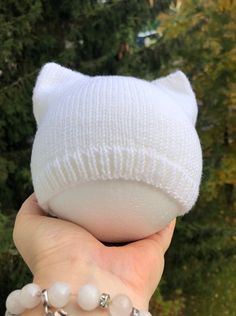 a hand holding a white cat hat with beads on it's wrist and bracelet