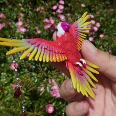 a red and yellow toy bird with its wings spread out in front of pink flowers