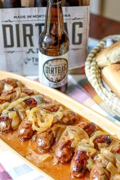 a hot dog bun with onions and sausage on it next to a bottle of beer