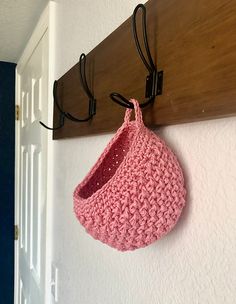 a pink crocheted purse hanging from a hook on a white wall next to a wooden coat rack