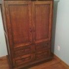 a wooden armoire in a room with hard wood flooring and white paint on the walls