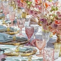 the table is set with pink flowers and gold plates, silverware, and napkins