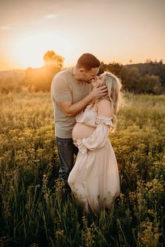 a pregnant couple kissing in a field at sunset